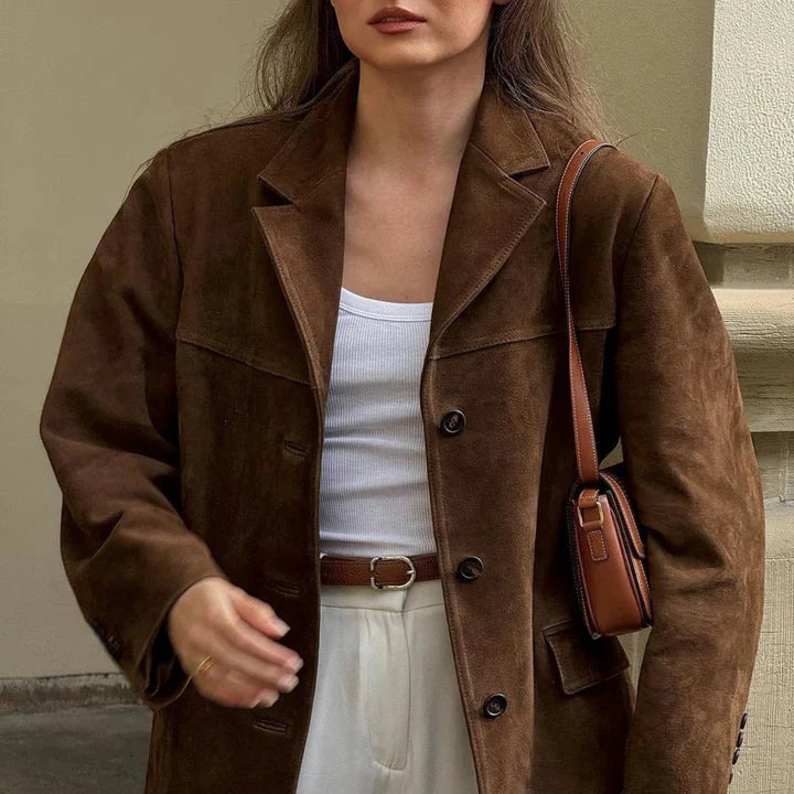 Women wearing a brown suede jacket with a white top and beige pants, holding a brown leather bag.