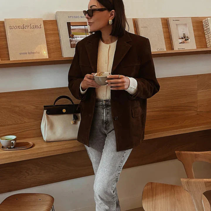 Woman in a brown coat holding a cup in a cafe setting